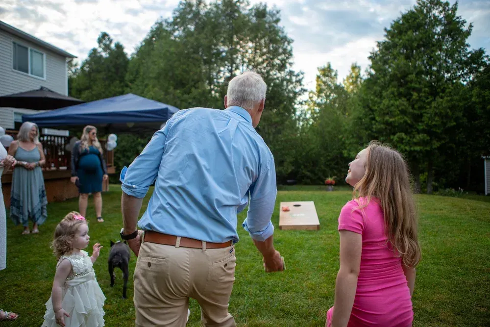 Guest mid-throw at a backyard cornhole game while a girl watches the toss