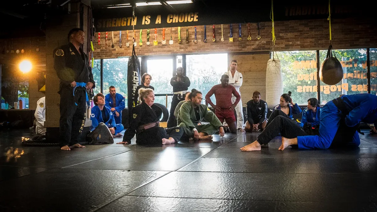 A jiu-jitsu class sitting on the mats listening, 'Strength is a choice' on the wall behind