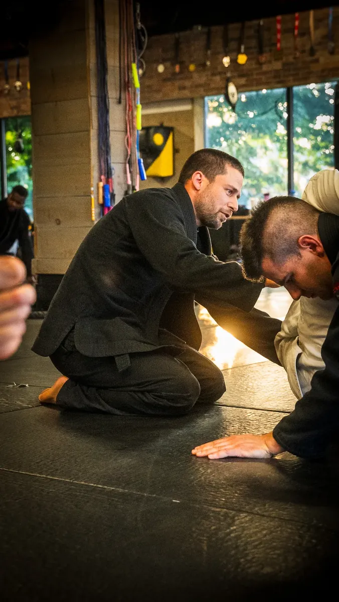 Jiu-jitsu instructor kneeling on the mats coaching a student through a technique