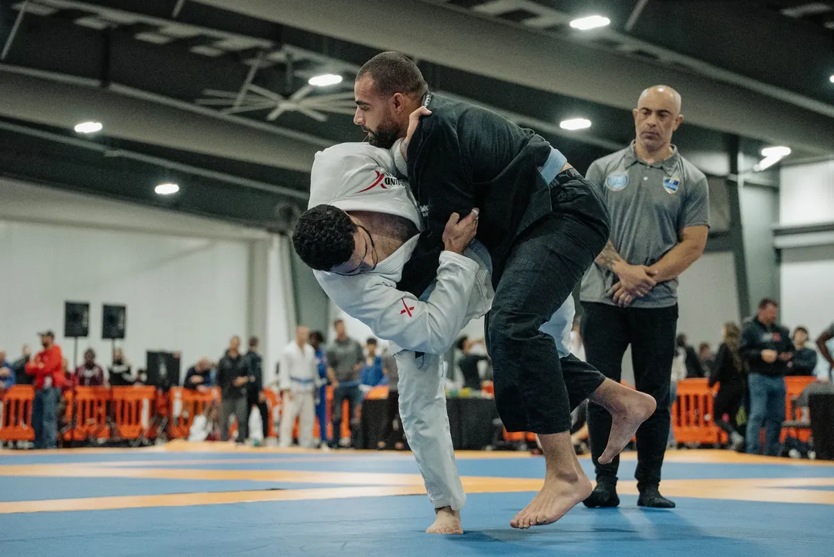 A throw landing mid-match in gi, the referee watching from a step away