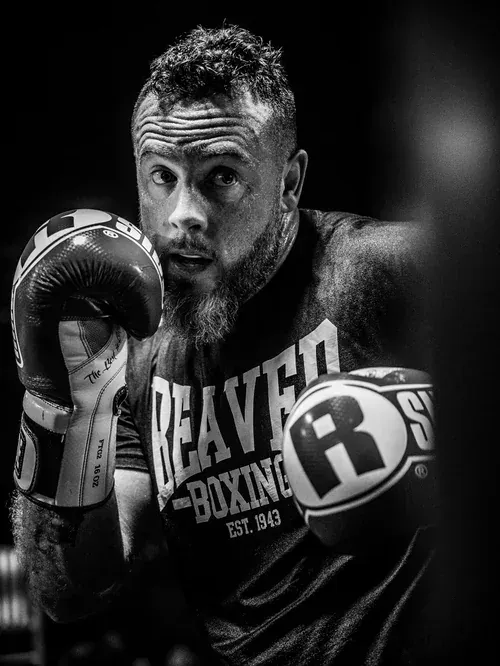 Boxer in a Beaver Boxing tee holding his guard, gloves up, in low gym light