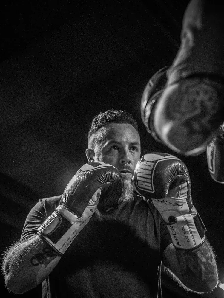 Close portrait of a boxer with both gloves raised, heavy bag swinging overhead