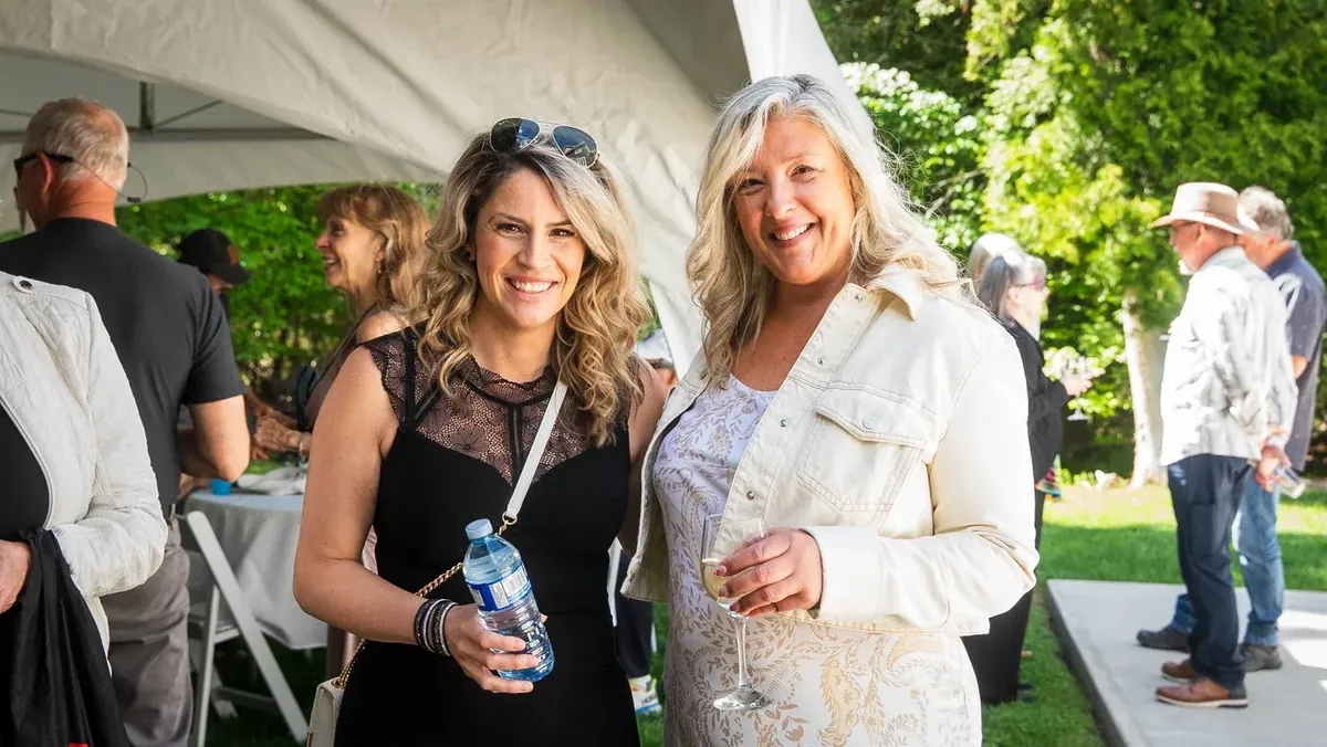 Two guests smiling together under a marquee at an outdoor event