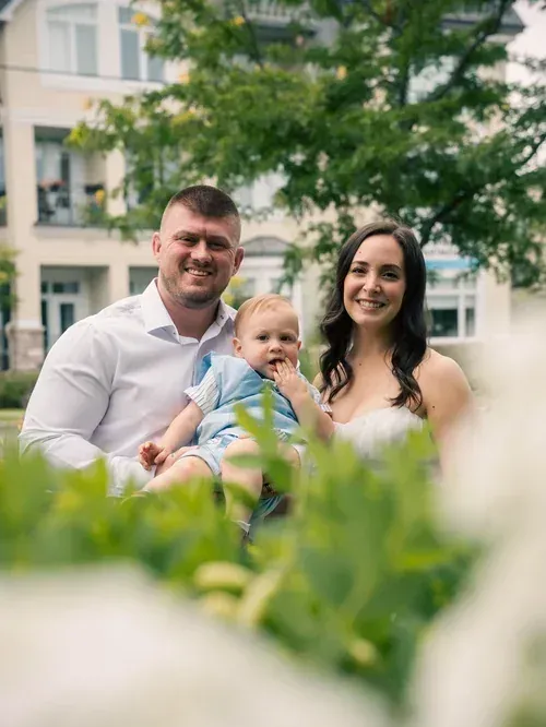 Parents sitting in the grass with their baby, foreground foliage softly blurred
