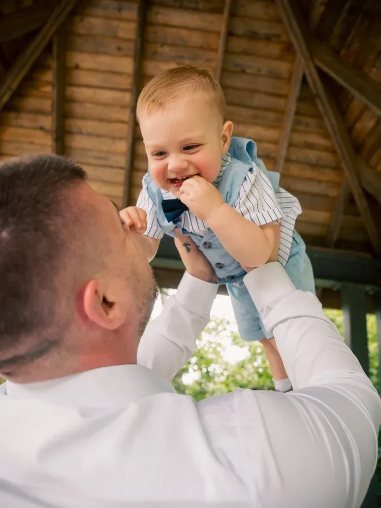 Father lifting his laughing baby overhead under a timber gazebo