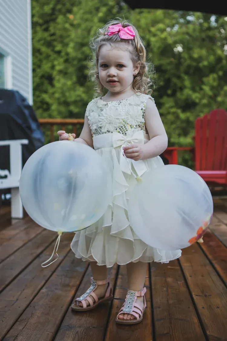 Flower girl in an ivory dress holding two oversized balloons on a deck