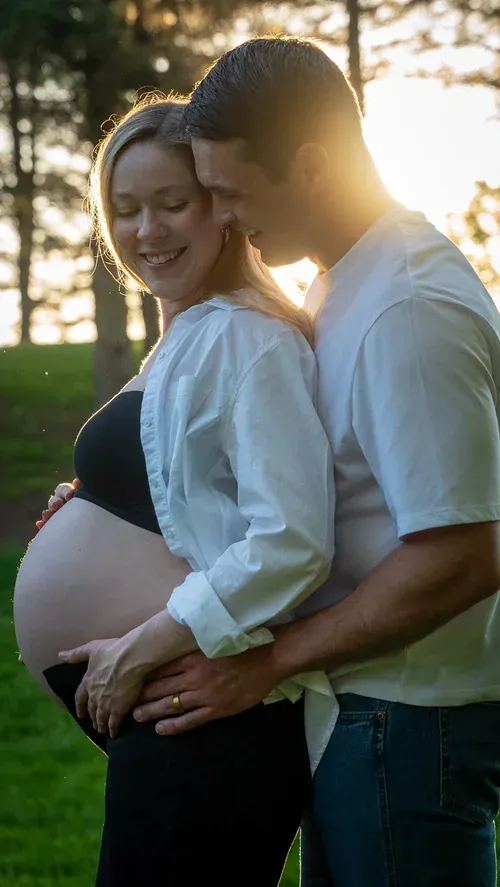 Expecting couple holding her bump, backlit by golden hour sun