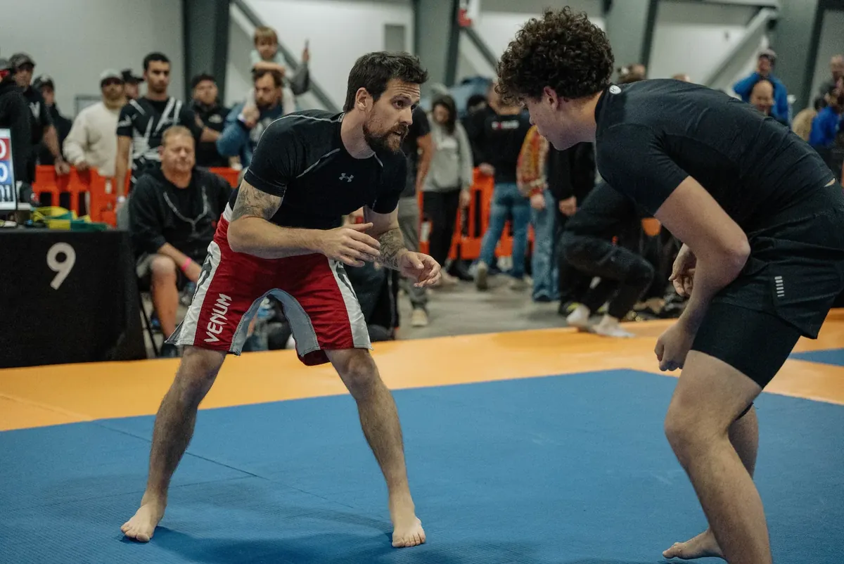 Two no-gi grapplers circling each other at the start of a match, crowd behind