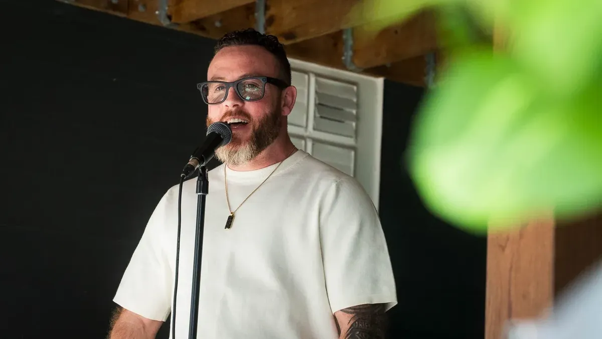Man giving a speech into a microphone, framed by leaves in the foreground