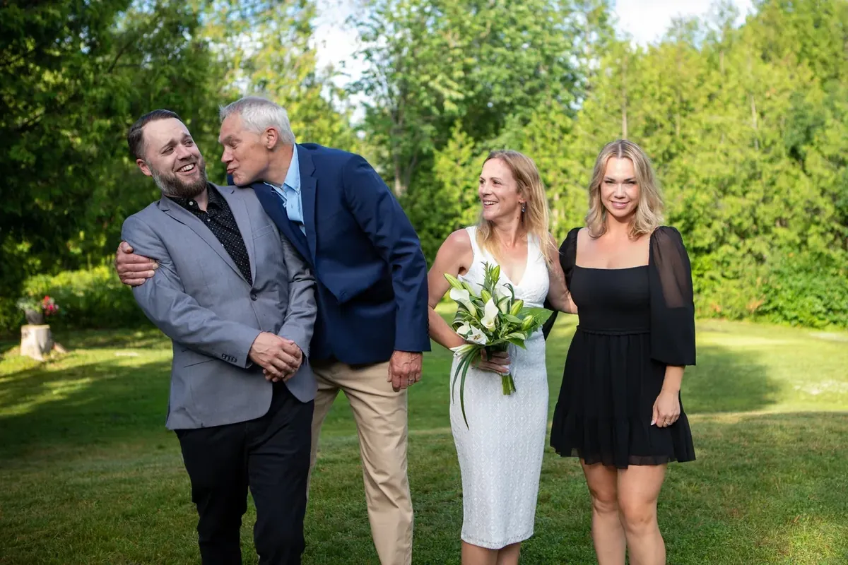 Wedding group of four laughing together on the lawn, bride holding calla lilies
