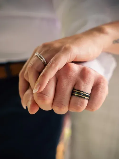 Close detail of two hands clasped, both wedding bands catching the light