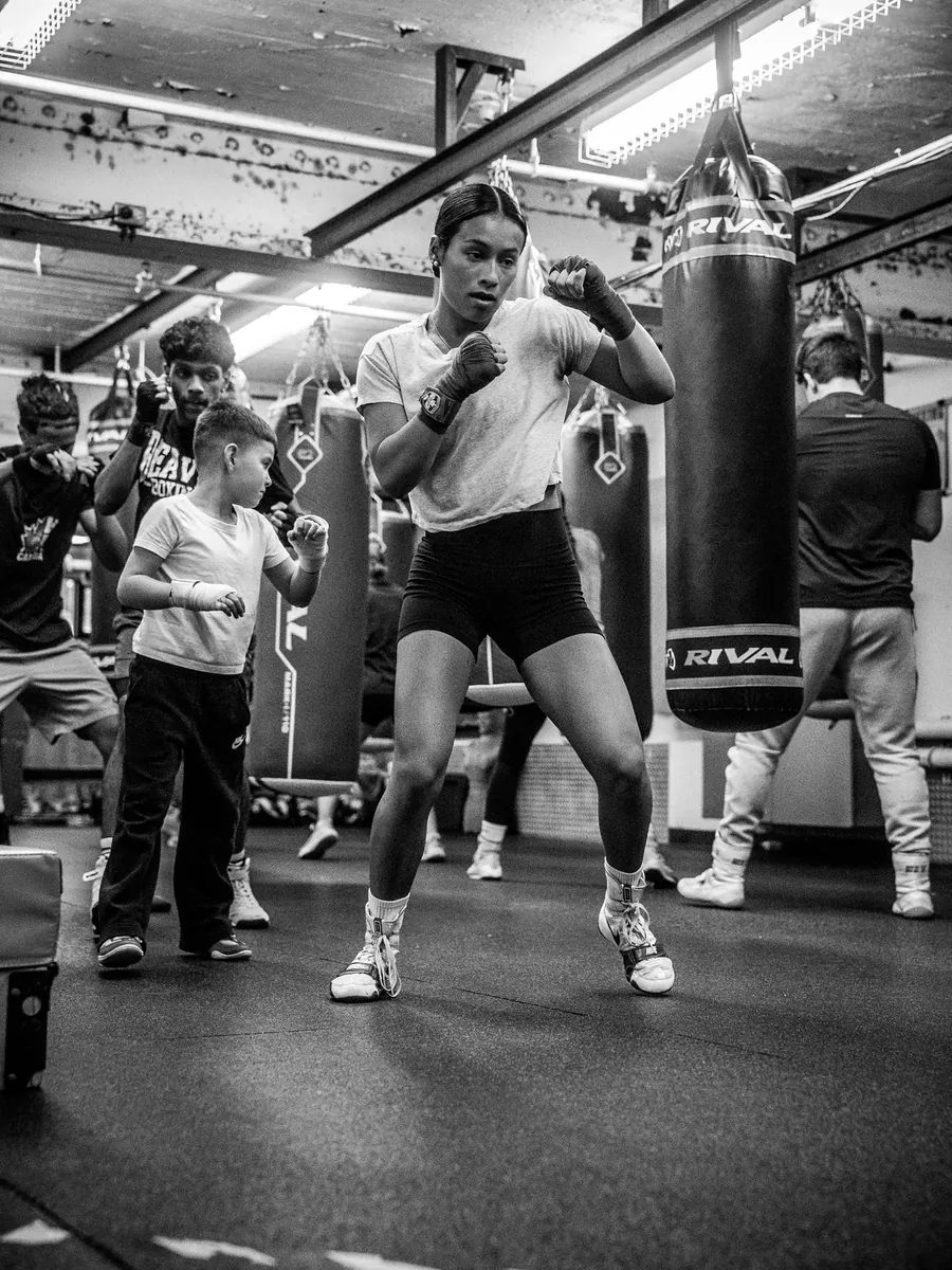 Boxer shadowboxing between the heavy bags, a young fighter mirroring her behind