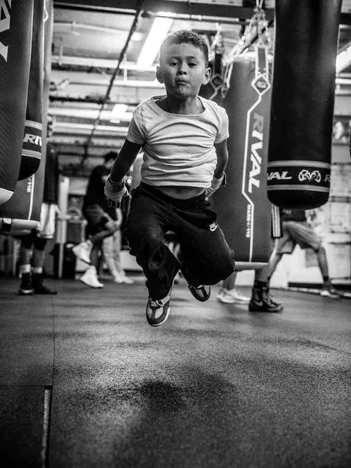 Young boxer caught mid-air skipping rope between heavy bags